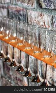 Glass champagne glasses lined up on a shelf diagonally near an old stone wall, whith copyspace for text.. Glass champagne glasses on a background of an old stone wall.