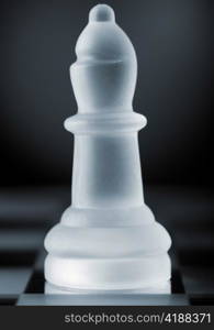 glass chess bishop is standing on board in dark