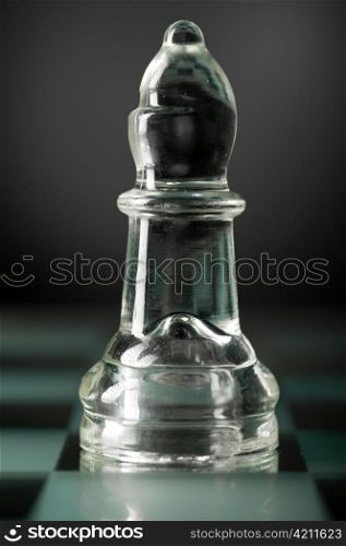 glass chess bishop is standing on board in dark