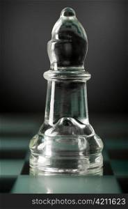 glass chess bishop is standing on board in dark