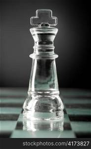 glass chess king is standing on board in dark