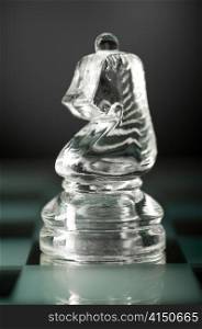 glass chess knight is standing on board in dark