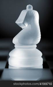 glass chess knight is standing on board in dark