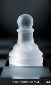 glass chess pawn is standing on board in dark