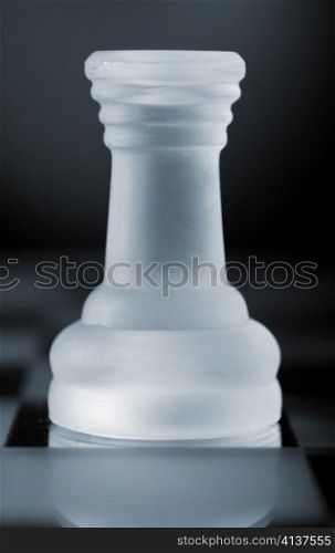 glass chess rook is standing on board in dark