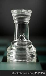 glass chess rook is standing on board in dark