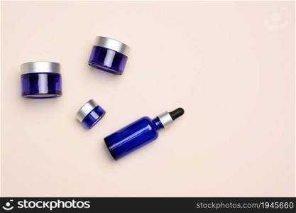 glass cosmetic blue bottles with a pipette and jar on a beige background. Cosmetics SPA branding mockup, top view
