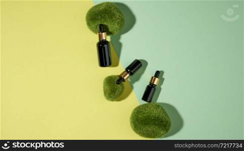 glass cosmetic brown bottles with a pipette on a green-yellow background with pieces of moss. Cosmetics SPA branding mockup, top view
