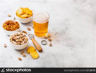 Glass craft lager beer with snack on stone kitchen background. Pretzel and crisps and pistachio in white ceramic bowl