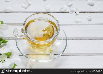 Glass cup of green tea and apple-tree flowers on white old wooden shabby background