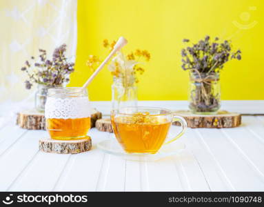 Glass cup of tea with linden in natural organic herbs and a jar of honey on a white wooden table. Increase immunity in the cool season.. Glass cup of tea with linden in natural organic herbs and a jar of honey on a white wooden table.