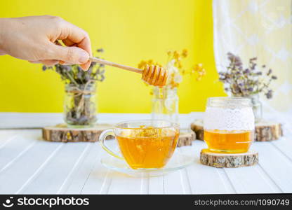 Glass cup of tea with linden in natural organic herbs and a jar of honey on a white wooden table. Increase immunity in the cool season.. Glass cup of tea with linden in natural organic herbs and a jar of honey on a white wooden table.