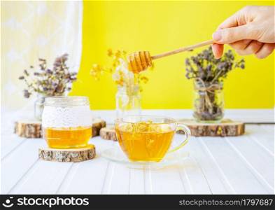 Glass cup of tea with linden in natural organic herbs and a jar of honey on a white wooden table. Increase immunity in the cool season.. Glass cup of tea with linden in natural organic herbs and a jar of honey on a white wooden table.