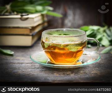 Glass cup with herbal sage tea on rustic table with books, close up
