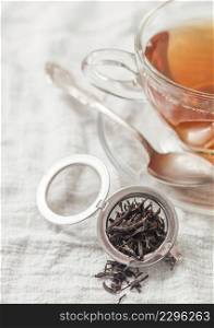 Glass cup with hot black tea and infuser with loose tea on white kitchen towel