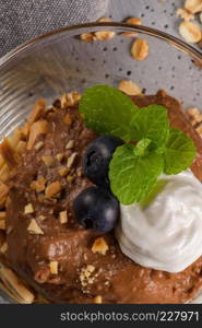 Glass cups of chocolate and chestnuts mousse with roasted almonds and oats decorated with black berries and mint leaves.