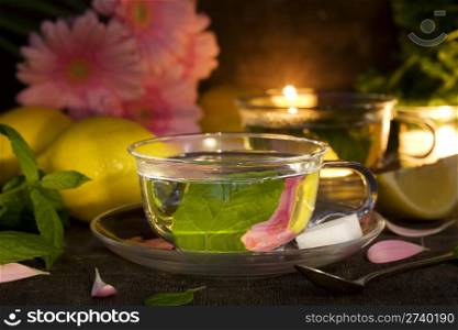 glass cups of mint tea with lemons and gerbera flowers (as decoration) on old rustic table