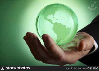 Glass green globe glowing in palm of businessmans hand