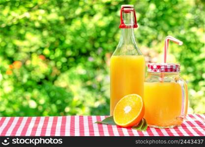 Glass jar and a bottle with orange juice. Half an orange with leaves. Natural green background. Glass jar and a bottle with orange juice