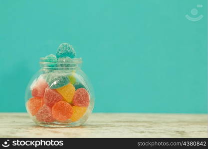 Glass jar full of jelly beans on a wooden table with blue background