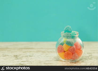 Glass jar full of jelly beans on a wooden table with blue background