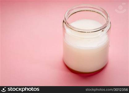 glass jar of coconut cooking oil on a pink background