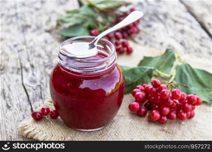 Glass jar of homemade viburnum jam with fresh viburnum berries on a wooden table. Source of natural vitamins. Used in folk medicine. Autumn harvest.. Glass jar of homemade viburnum jam with fresh viburnum berries on a wooden table. Source of natural vitamins. Used in folk medicine.