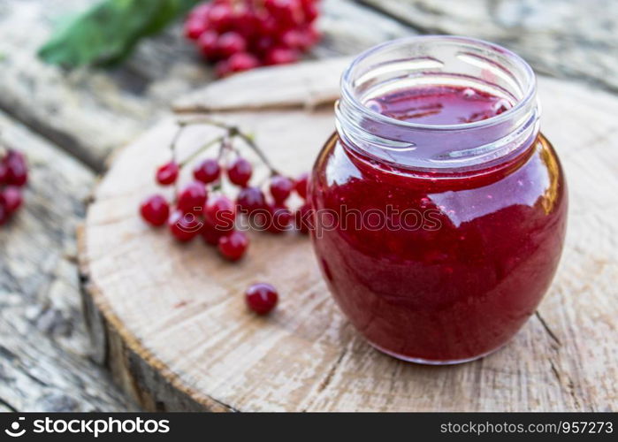 Glass jar of homemade viburnum jam with fresh viburnum berries on a wooden table. Source of natural vitamins. Used in folk medicine. Autumn harvest.. Glass jar of homemade viburnum jam with fresh viburnum berries on a wooden table. Source of natural vitamins. Used in folk medicine.