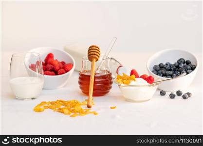 Glass jar of honey with dipper, surrounded by milk, cereal and assorted berries. Healthy lifestyle concept.. Milk and honey surrounded by cereal and berries