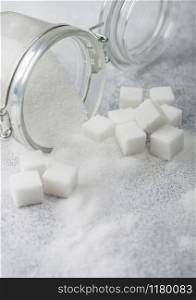 Glass jar of natural white refined sugar with cubes on light background.