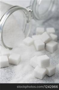 Glass jar of natural white refined sugar with cubes on light background.