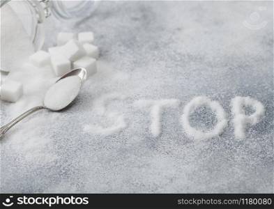Glass jar of natural white refined sugar with cubes with silver spoon on light background with STOp letters. Unhealthy food concept.