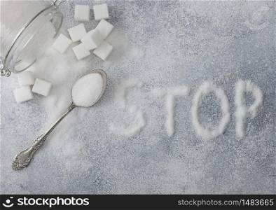 Glass jar of natural white refined sugar with cubes with silver spoon on light background with STOp letters. Unhealthy food concept.