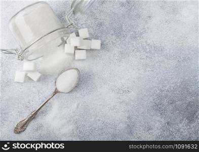 Glass jar of natural white refined sugar with cubes with silver spoon on light background. Space for text