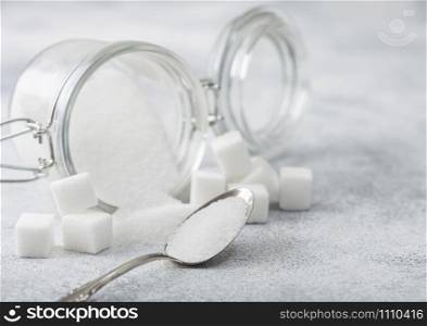 Glass jar of natural white refined sugar with cubes with silver spoon on light background.