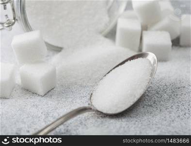 Glass jar of natural white refined sugar with cubes with silver spoon on light background. Macro