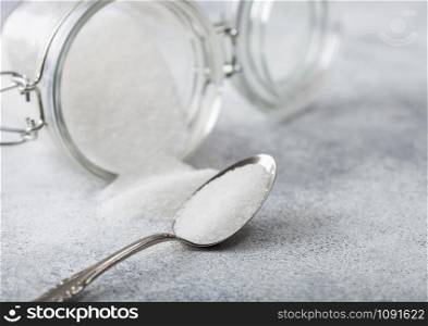 Glass jar of natural white refined sugar with silver spoon on light background.