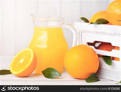 Glass jar of organic fresh orange juice with raw oranges in white wooden box