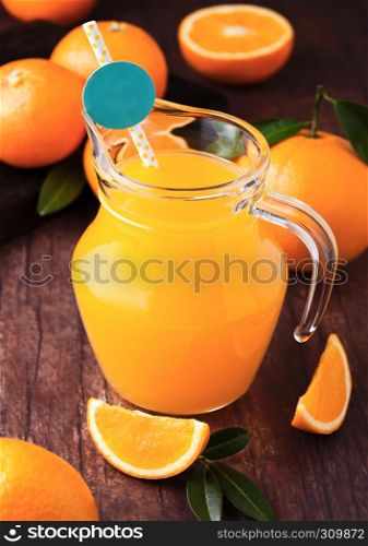 Glass jar of organic fresh orange juice with raw oranges on dark wooden background