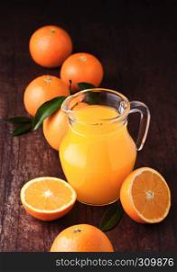 Glass jar of organic fresh orange juice with raw oranges on dark wooden background