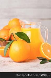 Glass jar of organic fresh orange juice with raw oranges on light wooden background