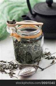 Glass jar of organic loose green tea with vintage metal strainer infuser on light background with Japanese Iron Teapot and green cloth.