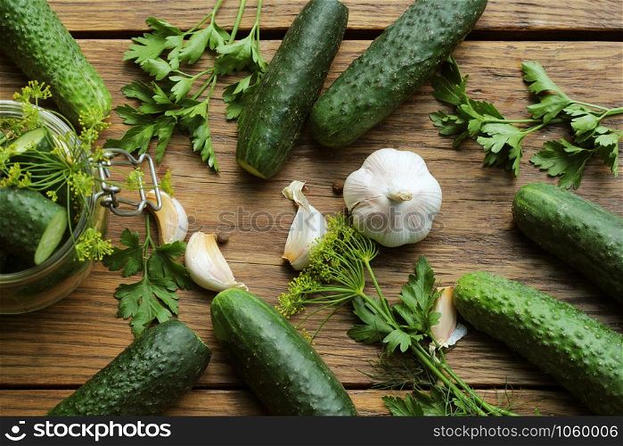 Glass jar of pickled cucumbers with herbs on rustic wooden background. Marinated and canned food. Top view .. Glass jar of pickled cucumbers with herbs on rustic wooden background. Marinated and canned food. Top view