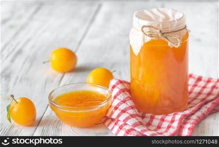 Glass jar of plum jam with fresh plums on the wooden background