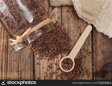 Glass jar of raw natural organic linseed flax-seed with spoon and linen cloth on wood background.Top view