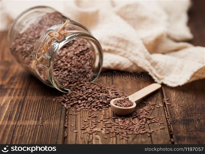 Glass jar of raw natural organic linseed flax-seed with spoon and linen cloth on wood background.