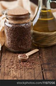 Glass jar of raw natural organic linseed flax-seed with spoon and oil on wood background. Healthy omega 3 product.