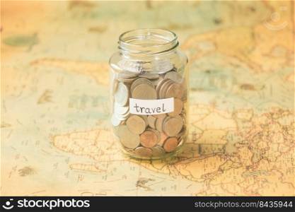 Glass jar with coins and travel inscription on world map on table. Travel concept and saving money.