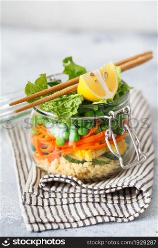 Glass jar with fresh raw vegetables and couscous groats. Healthy Meal Prep - recipe preparation photos. Healthy vegan dishes in glass containers. Weight loss food concept. Salad in a jar with chopsticks.