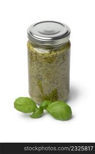 Glass jar with green Italian pesto and fresh basil leaves in front isolated on white background
